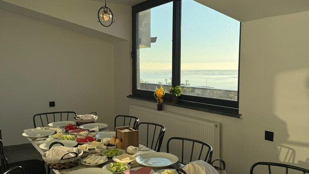 A dining area with a table set for a meal, chairs, a window with a view, and a ceiling light. - Koç Guest House (Demirkoy)