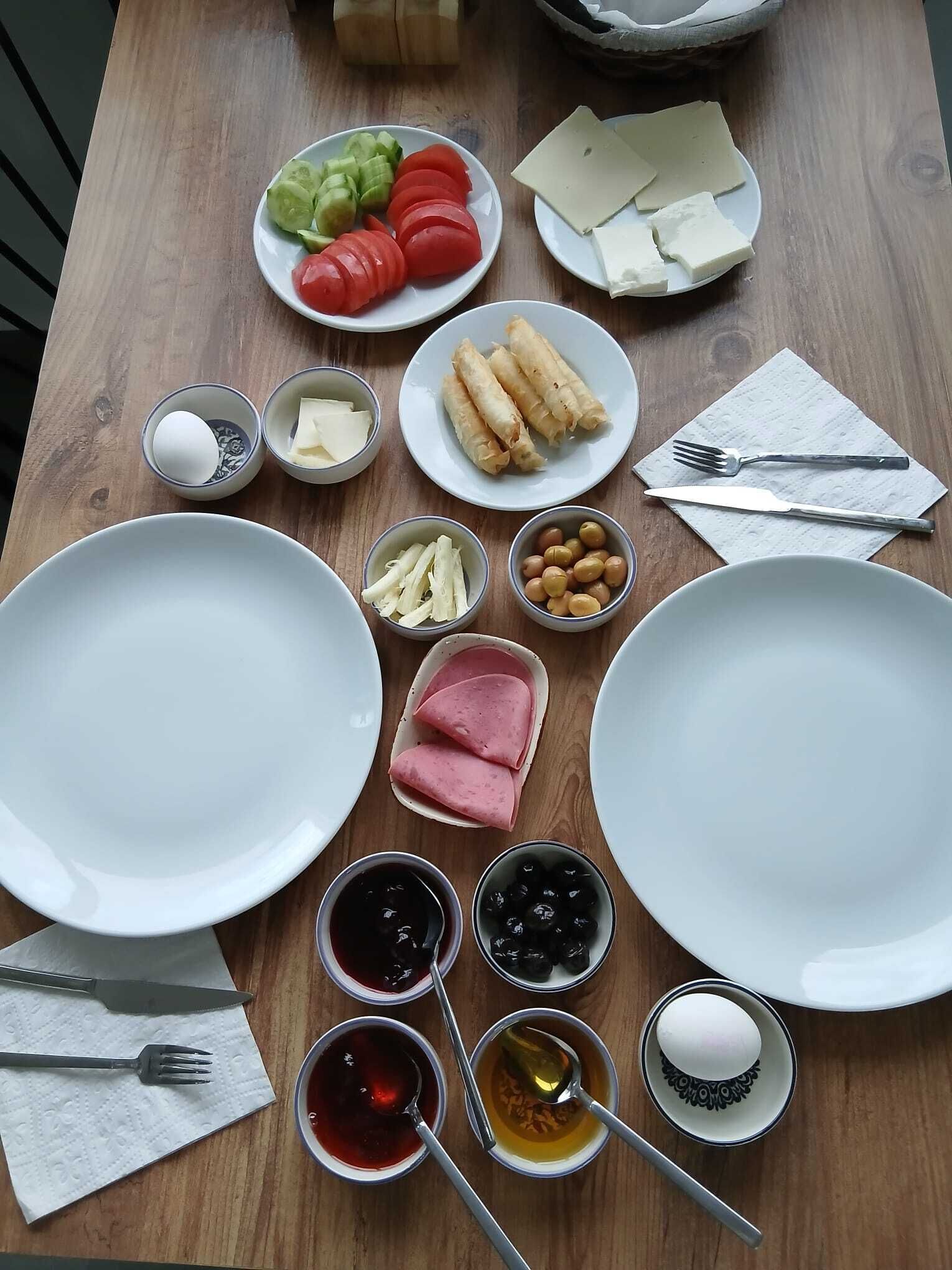A wooden table with various food items and utensils, including plates, bowls, and a knife and fork set.