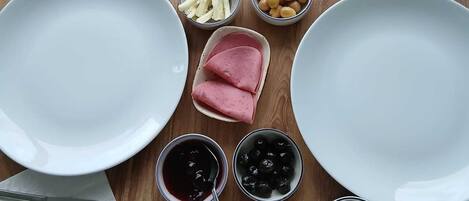 A wooden table with various food items and utensils, including plates, bowls, and a knife and fork set.