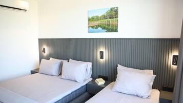 Ein Hotelzimmer mit zwei Betten, einer Wand-Klimaanlage, einem Nachttisch mit einem Buch und einem Bilderrahmen mit einem Seeblick.