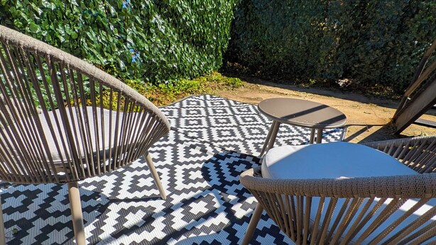 A patio area with patterned flooring, wicker chairs, and a view of a residential building in the background.