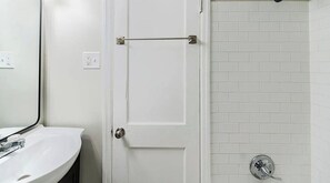 A bathroom with a white sink, a door with a towel bar, and a shower area with white tiles.