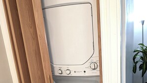 A laundry room with a white washer and dryer, wooden door frame, and a potted plant in the corner.