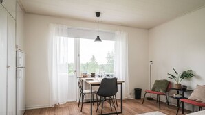 A room with a dining table, chairs, a sofa, a floor lamp, and a potted plant.