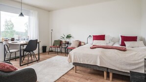 A bedroom with a bed, bedside tables, a desk, chairs, a floor lamp, and a window.