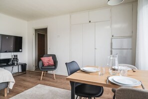 Quarto moderno e bem iluminado, com uma mesa de jantar posta para dois, televisão e uma área de cozinha compacta.