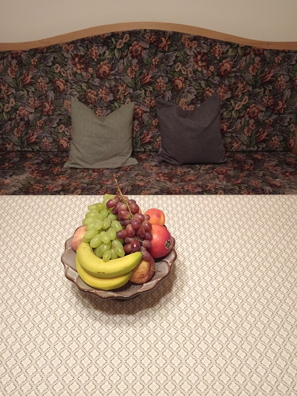 A fruit bowl on a table with a floral sofa in the background.