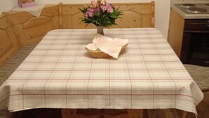 Una mesa de comedor con mantel a cuadros, un florero con flores y una cesta sobre la mesa.