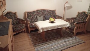 Una habitación acogedora con techo de madera, un sofá floral, un sillón a juego, una mesita con frutero y una lámpara de pie.
