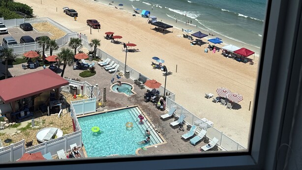 Une vue sur la plage avec une piscine, des parasols et des chaises longues.
