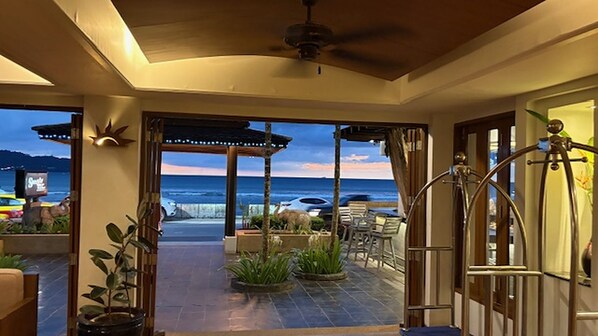 A covered outdoor area with a view of the ocean, a patio with chairs, and a ceiling fan.