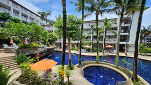 A hotel pool area with multiple pools, lounge chairs, and palm trees. - Fantastic apartment with AC and great pool in Kalim Patong by the Sea (Tambon Patong)
