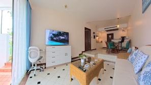 A modern living room with a flat-screen TV, a sofa, a dining area, and a kitchen.