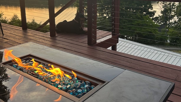 A deck with a fire feature and a view of a lake at sunset.