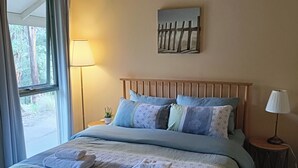 Une chambre à coucher avec un lit, des oreillers, une lampe, un tableau et une fenêtre.
