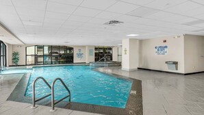 An indoor swimming pool with a lifeguard station, a sign indicating no lifeguard on duty, and a poolside area with a trash can.