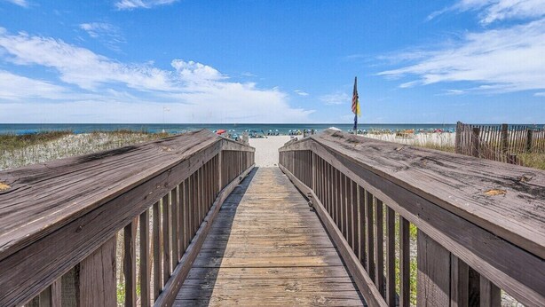 A wooden boardwalk leading to a beach with a flag on the right.