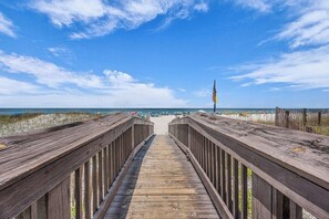 A wooden boardwalk leading to a beach with a flag on the right.