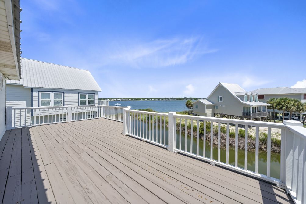 A wooden deck with white railings overlooking a body of water and a distant shoreline.