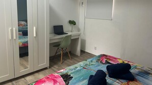 Ein Schlafzimmer mit Bett, Schreibtisch mit Laptop, Stuhl und Kleiderschrank.