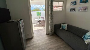 Ein kompakter Wohnbereich mit Küchenzeile, einer Couch, einer Essecke mit Tisch und Stühlen sowie einem Fenster mit Vorhängen.