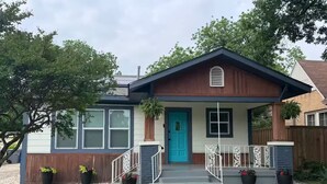 Una casa de un piso con puerta azul, un pequeño porche con barandillas blancas y un buzón.