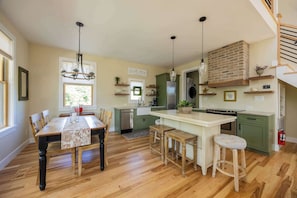 A modern kitchen with wooden flooring, a central island, bar stools, and a dining table.