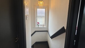 A narrow stairway with a window at the top, a hanging light fixture, and a small potted plant on the windowsill. - Daisy Haven in Southampton (Southampton)