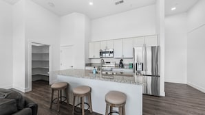 A modern kitchen with white cabinets, stainless steel appliances, and a granite countertop. There are three stools at the island and a door leading to a storage area. - Welcoming 3-bedroom suite in Gardnerville, NV near Topaz Lake. (Gardnerville)
