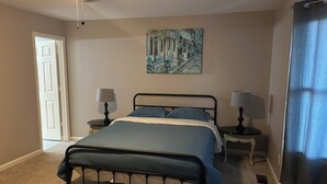 Ein Schlafzimmer mit einem Bett, zwei Nachttischen mit Lampen, einem Deckenventilator, einer Tür und einem Bild an der Wand.