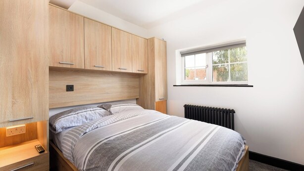 Une chambre à coucher avec un lit, une armoire en bois, une fenêtre et un radiateur.