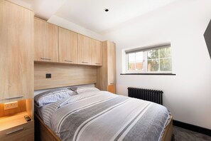 A bedroom with a bed, wooden wardrobe, a window, and a radiator. - A stylish Modern 200 Year Old - 2 Bedroom cottage! (Redbourn)