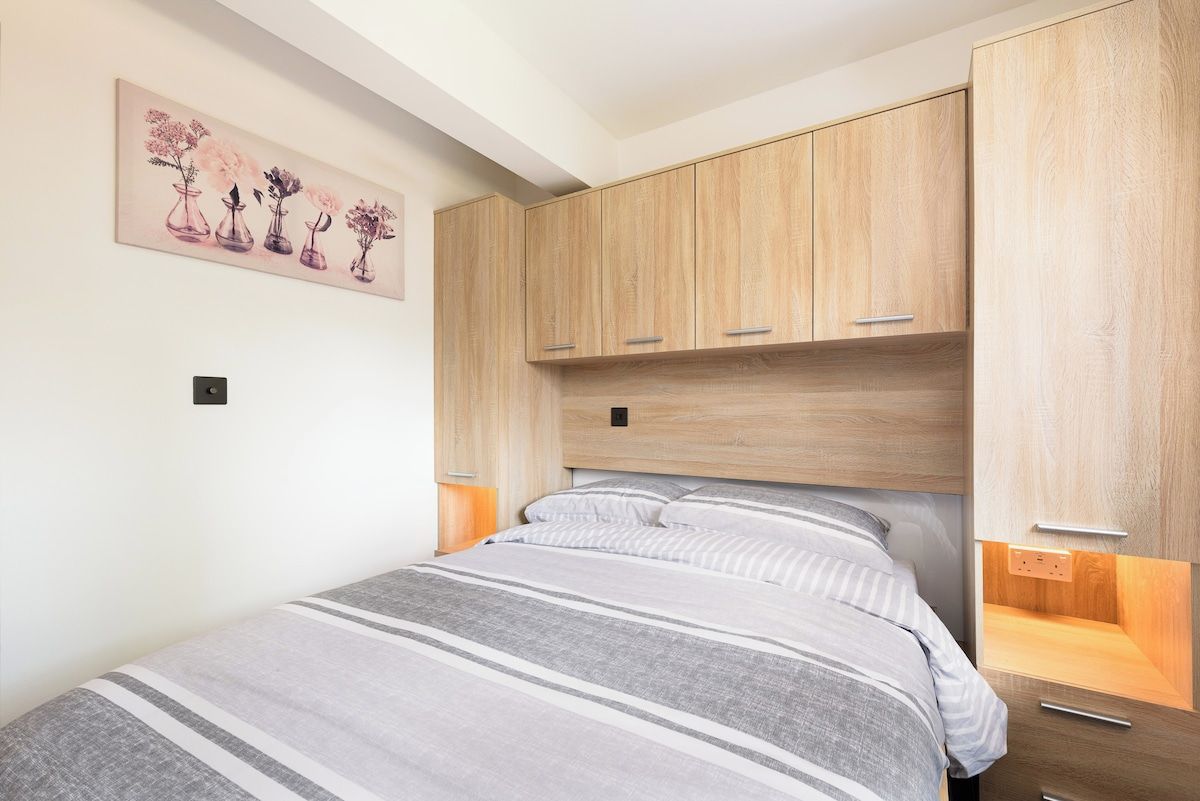 Une chambre à coucher comprenant un lit, une armoire en bois, des tables de chevet et une œuvre d’art à motifs floraux accrochée au mur.