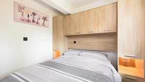 Quarto com cama, guarda-roupa de madeira, mesas de cabeceira e uma obra de arte floral na parede.