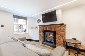 Una sala de estar con chimenea de ladrillo, un televisor de pantalla plana montado encima y un sofá con cojines estampados.