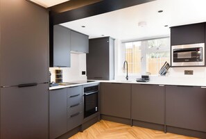 Una cocina moderna con armarios oscuros, horno empotrado y ventana que proporciona luz natural.