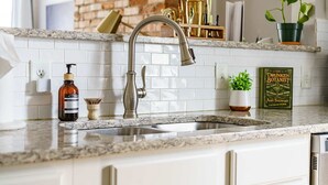 A kitchen with a stainless steel sink, a marble countertop, a book titled 'The Drunken Botanist,' and a potted plant. - Short North & Downtown & OSU | Near High Street | Free Parking | 5,800+ Reviews (Columbus)