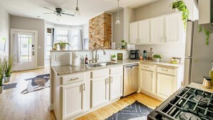A modern kitchen with white cabinets, a brick accent wall, a gas stove, and various kitchen appliances. - Short North & Downtown & OSU | Near High Street | Free Parking | 5,800+ Reviews (Columbus)