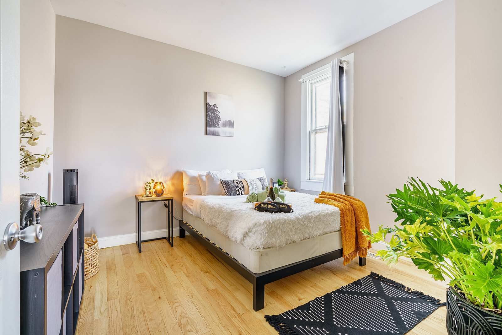 A bedroom with a bed, bedside tables, a window, and a potted plant.