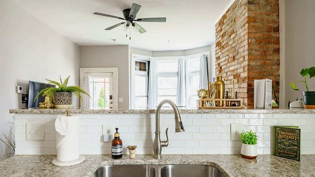 A kitchen with a double sink, a ceiling fan, a brick wall, and a window. - Short North & Downtown & OSU | Near High Street | Free Parking | 5,800+ Reviews (Columbus)