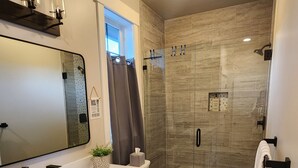 A modern bathroom with a white vanity, a large mirror, a shower with glass doors, and a bathtub. - Lake Chelan view home 1-bedroom in Manson with AC (Manson)