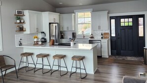 A spacious kitchen with white cabinetry, a central island with bar stools, a ceiling fan, and a black door. - Lake Chelan view home 1-bedroom in Manson with AC (Manson)