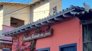 Ein Gebäude mit rosafarbenem Mauerwerk, blauen Fensterläden und einem Schild mit der Aufschrift 'Pousada Recanto da Praia'.