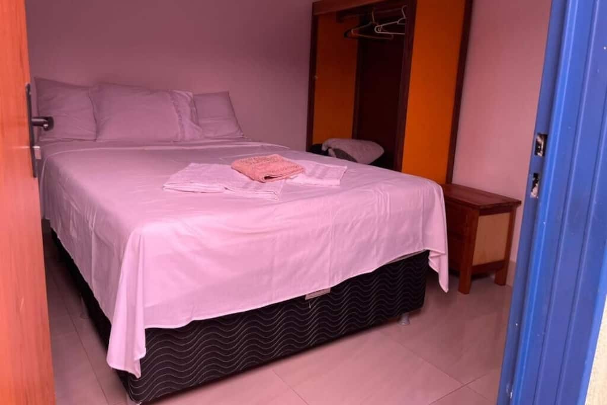 Un dormitorio con cama, mesita de noche, armario y puerta.