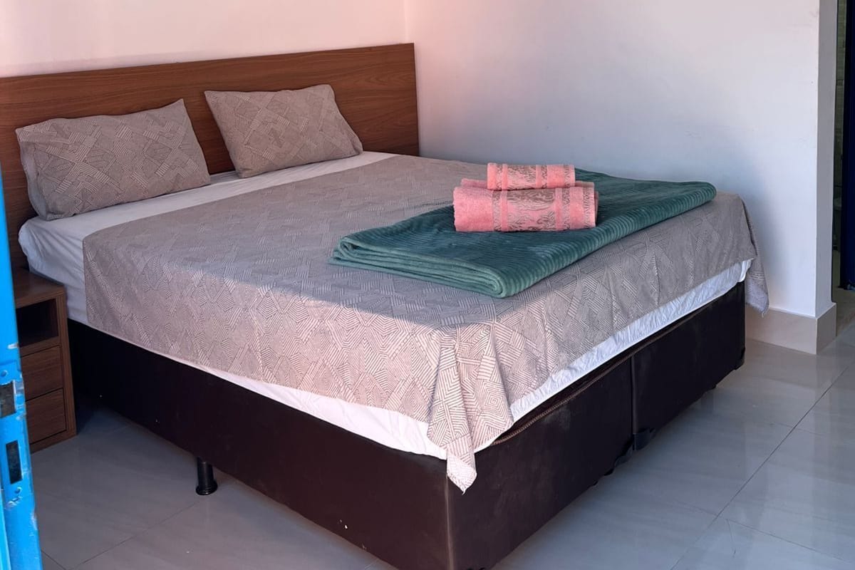Una cama bien tendida con un edredón estampado, dos almohadas y toallas dobladas.