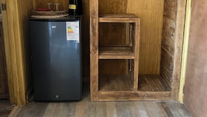A compact kitchen with a refrigerator, a wooden shelf unit, and a hanging coat rack. - Hostal Lago Cóndor (Natales)