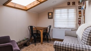 A cozy room with a skylight, a dining table with chairs, a radiator, and a checkered sofa. - Hostal Lago Cóndor (Natales)
