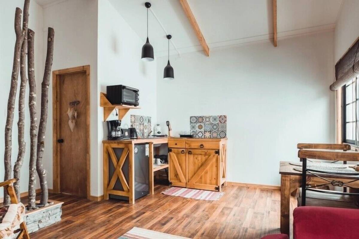 A rustic kitchen with wooden cabinets, a built-in dishwasher, and a small countertop. There are wooden beams on the ceiling and a window with a view of the outdoors.