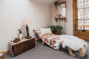 A cozy room with a bed, a wooden bench, a lamp, and a mirror. - Hostal Lago Cóndor (Natales)
