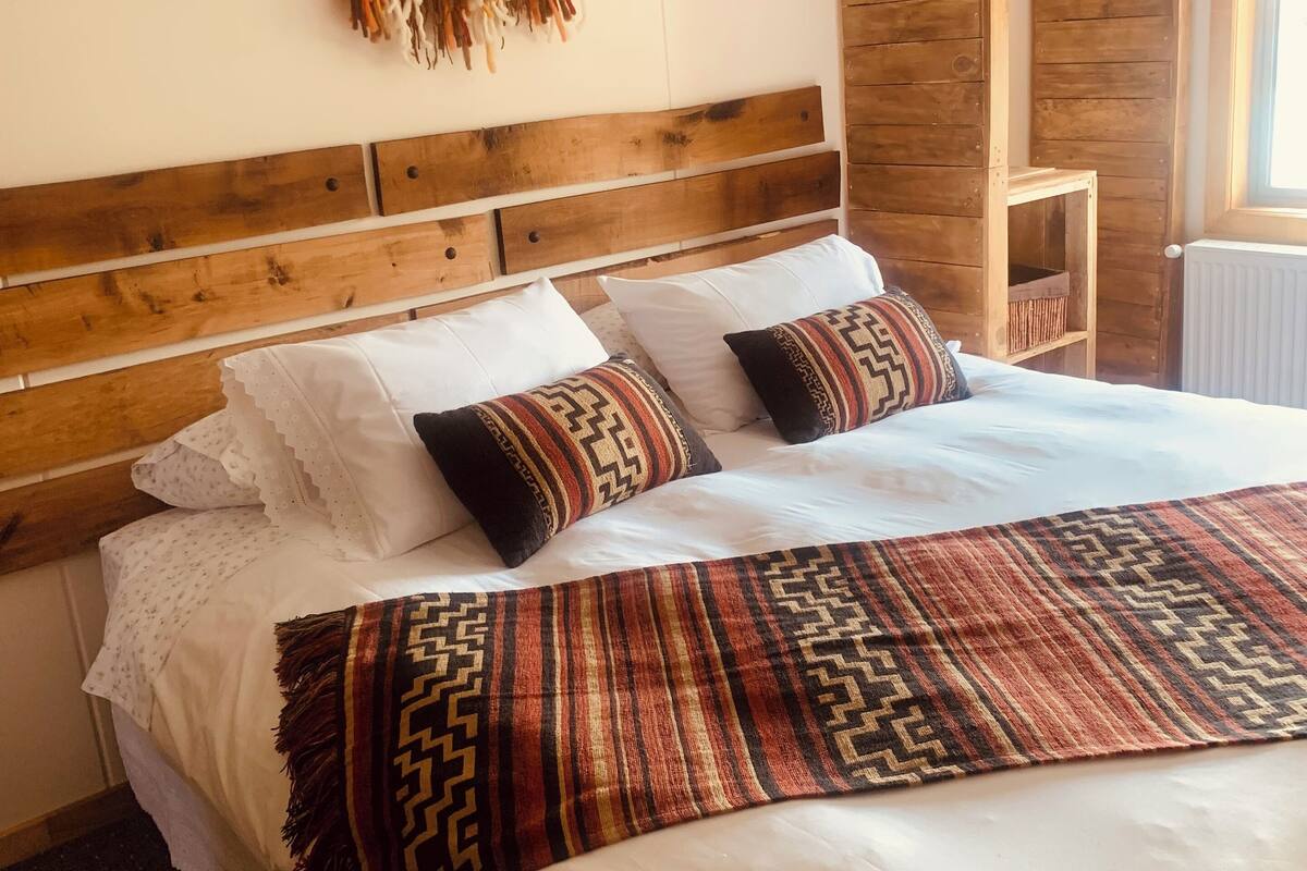 A bed with a wooden headboard, white bedding, patterned pillows, and a decorative wall piece.